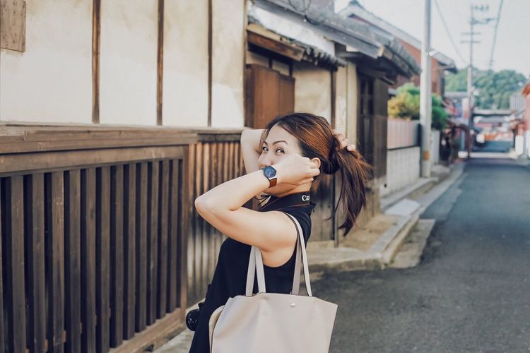 Side view portrait of woman adjusting hair while standing on street