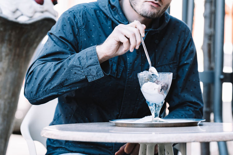 Midsection of man eating ice cream at cafe