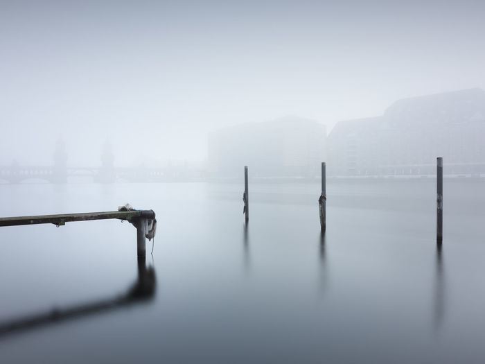 Wooden posts and jetty amidst calm lake during foggy weather