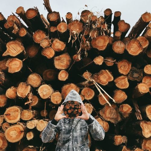 Man holding picture frame while standing against stack of logs