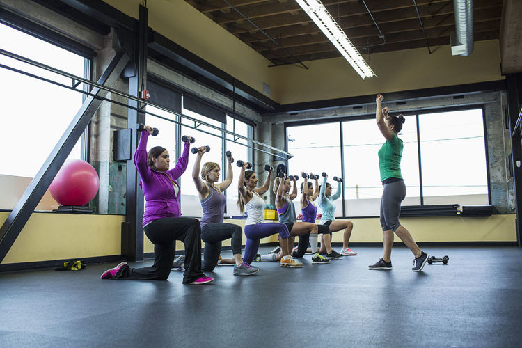 Fitness instructor guiding women in lifting dumbbells at gym