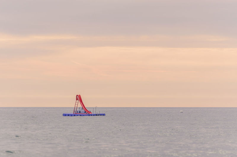 Slide on diving platform in sea against sky during sunset