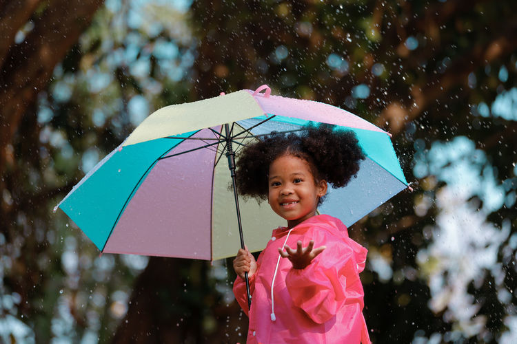 Portrait of smiling girl holding umbrella standing during rainy season
