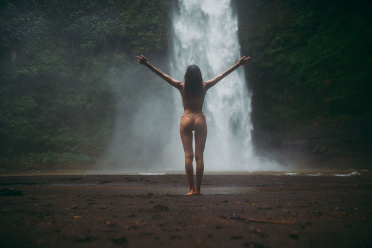 Rear view of woman standing at waterfall