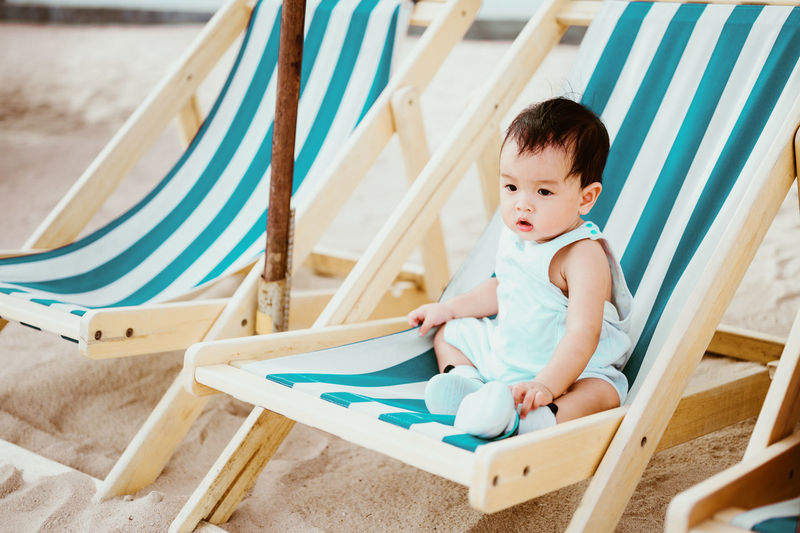 Cute baby boy sitting on chair at beach