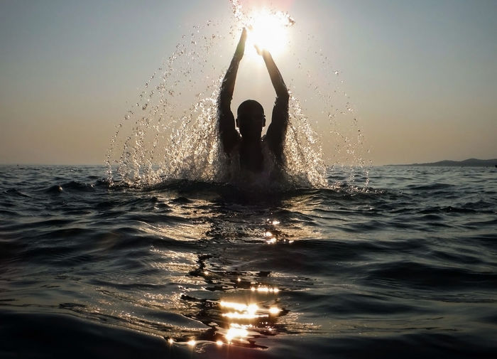 Silhouette woman splashing water in sea against sky during sunset