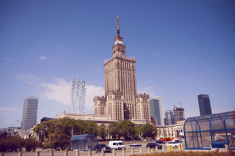 Palace of culture and science by street against blue sky