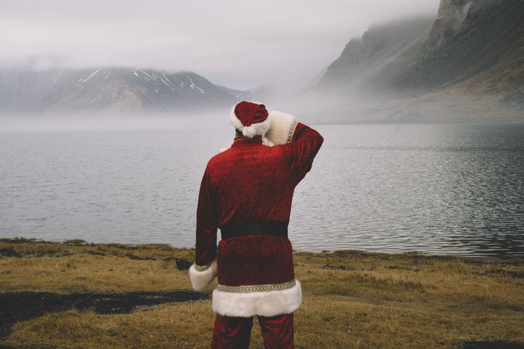 Rear view of man wearing santa claus costume looking at lake during foggy weather