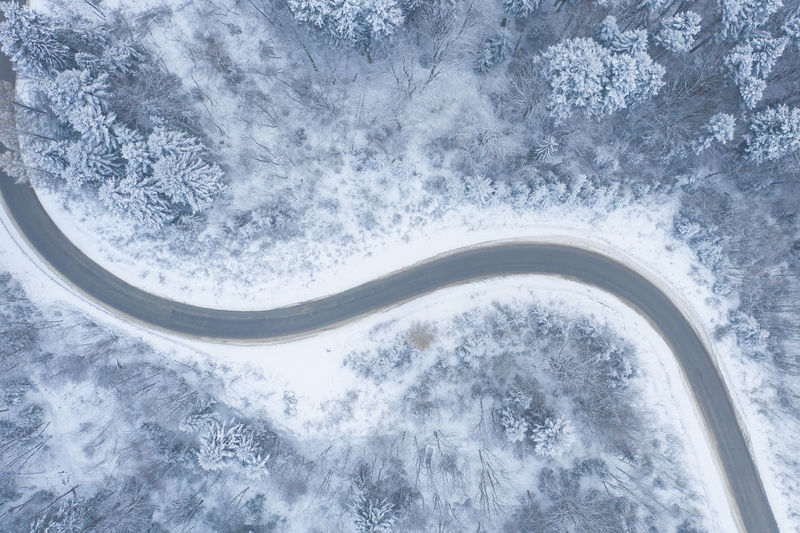 Aerial view of winter road and forest with snow covered trees, top view/