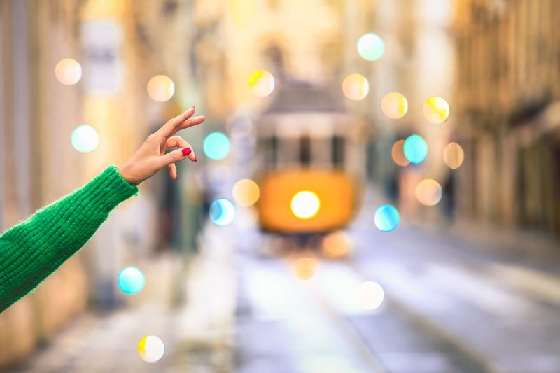 Cropped hand of woman hailing cable car on road in city