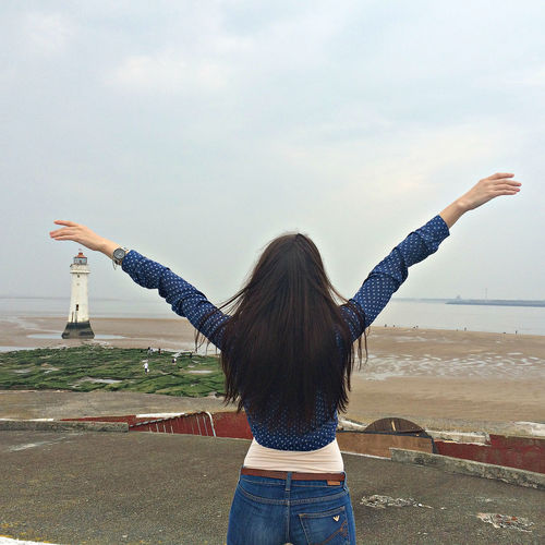 Rear view of woman with arms outstretched standing against sky