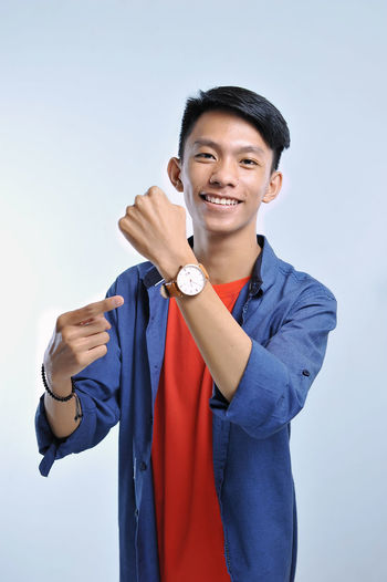 Potrait of handsome young asian man pointing to the wristwatch with pretty smiling