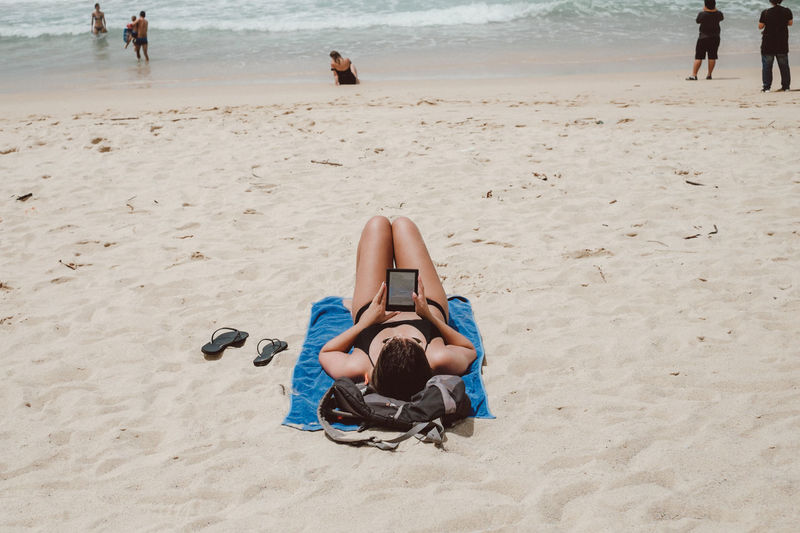 Woman using digital tablet while lying at sandy beach
