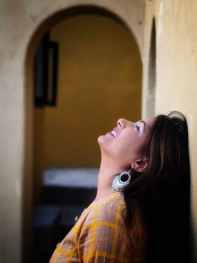 Side view of smiling young woman standing by wall