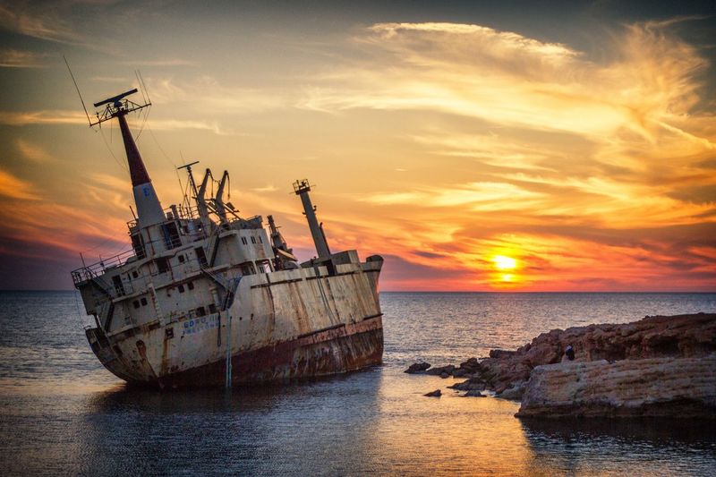 Abandoned ship in sea against sky during sunset