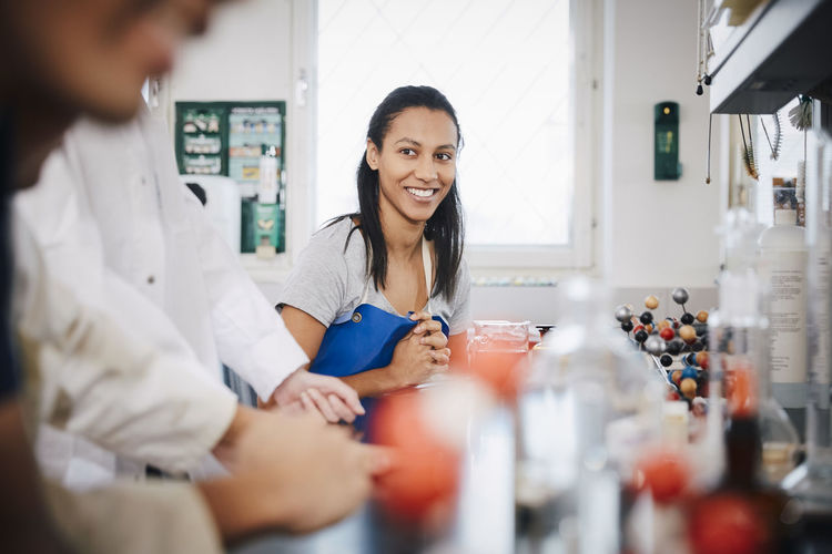 Confident female student looking at friends sitting in chemistry laboratory