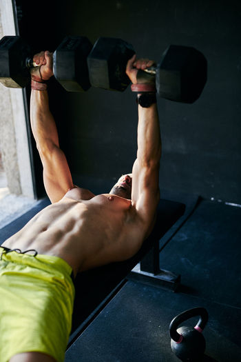 Shirtless fit young man working out in a garage with dumbells