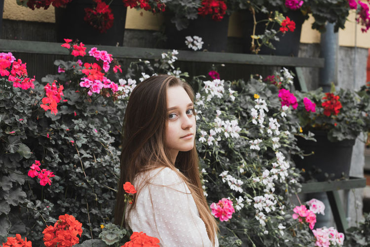 Portrait of young woman standing by flowering plants