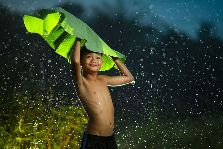 Shirtless boy holding banana leaf during rainy season