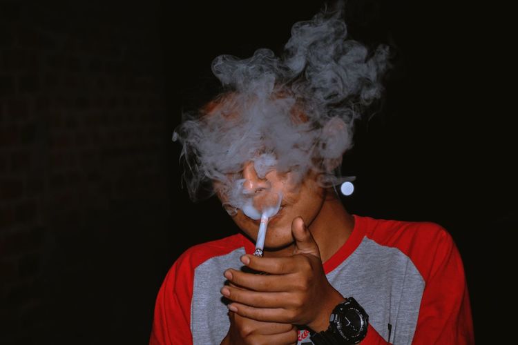 Portrait of man smoking against black background
