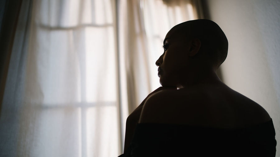 Side view of tranquil african american female with bald hairstyle and in towel at home and looking away