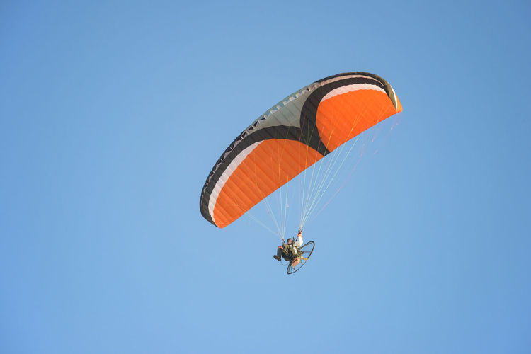 Low angle view of young man motor paragliding against clear sky