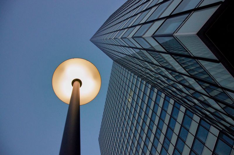 Low angle view of illuminated street light by modern building against clear sky