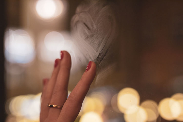 Cropped hand of woman making heart shape on glass