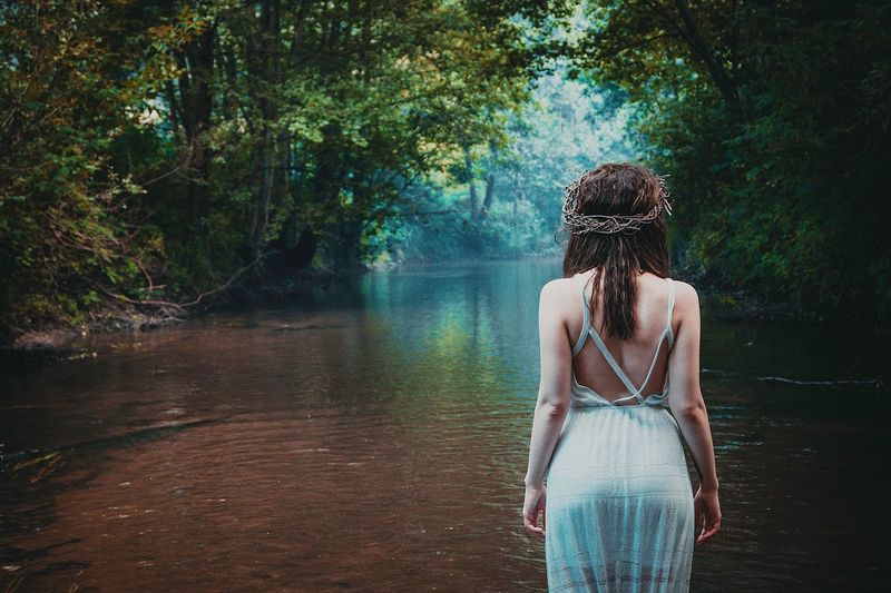 Rear view of woman standing by stream in forest