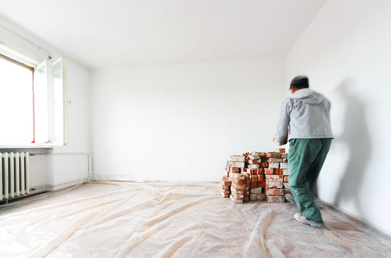 Rear view of man arranging bricks by wall at home during renovation