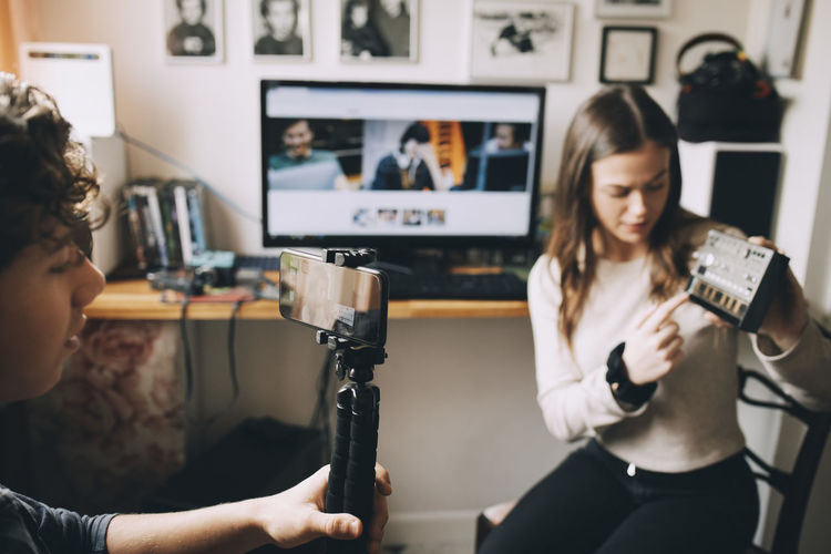 Teenage boy filming friend using sound mixer on monopod while sitting at home