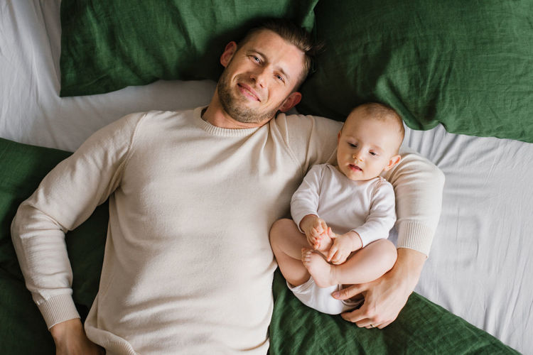 A cheerful, beautiful newly-made dad and a charming six-month-old baby lie together 