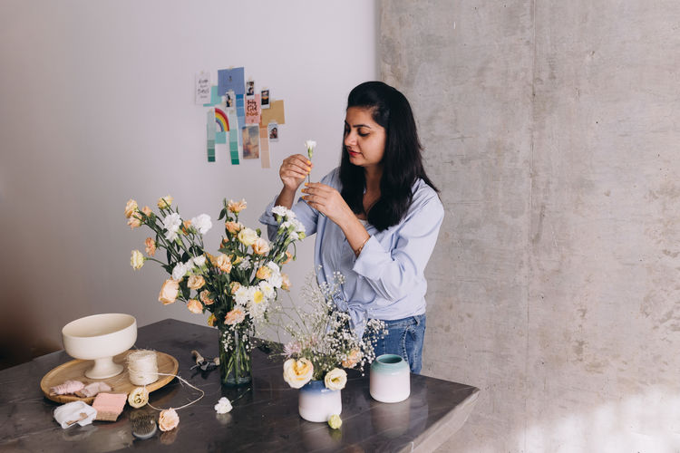 Florist of indian ethnicity  standing in front of a table creating a bouquet of flowers