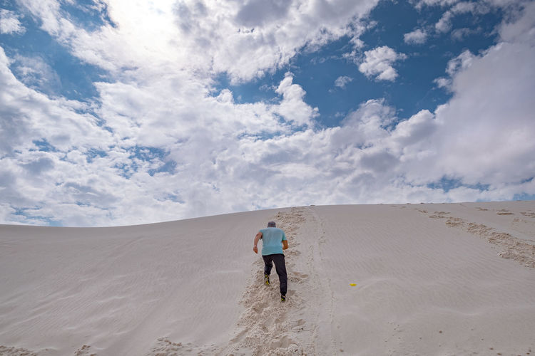 Rear view of man climbing in sand dune against sky