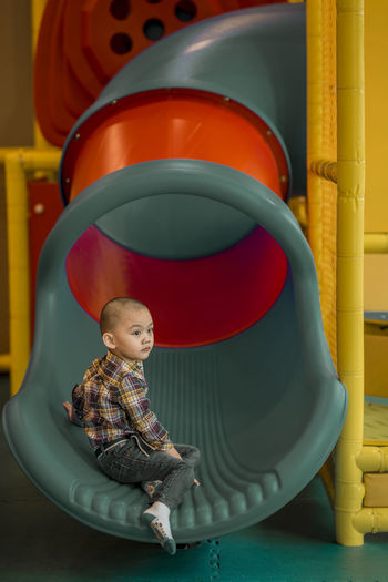 Side view of cute boy looking away while sitting on slide
