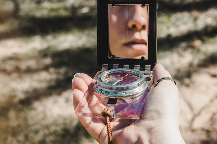 Close-up of young woman holding compass with reflection in mirror