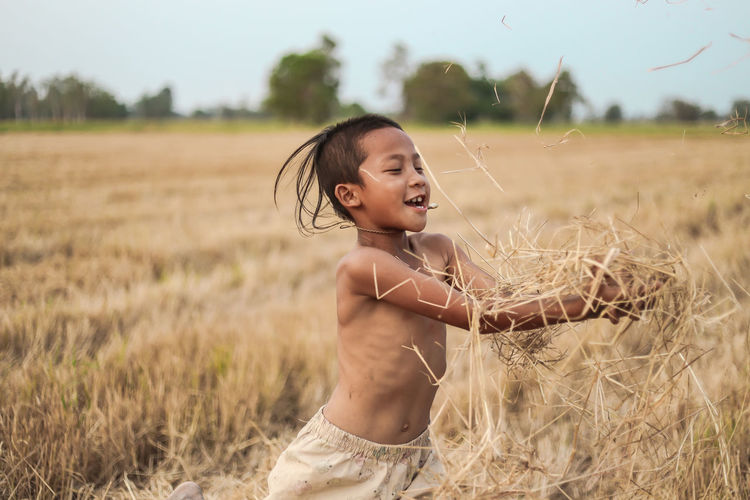 Boy playing with straws while standing on field at farm against sky