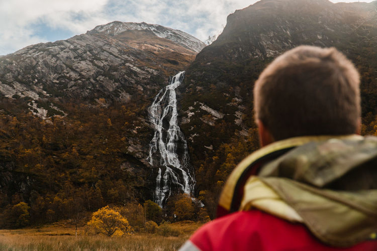 Over shoulder view of male looking at waterfall and mountains in scotland at winter. 
