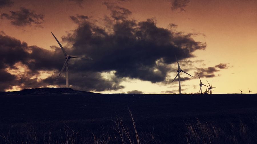 Wind turbines on silhouette landscape against sky