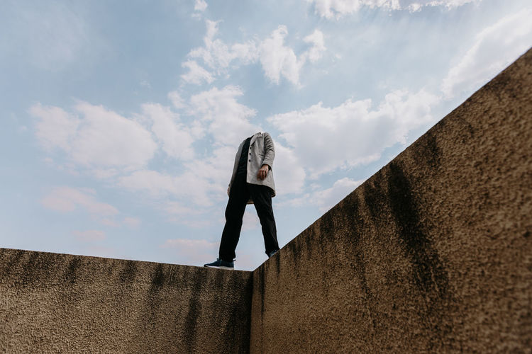 Low angle view of man standing on wall against sky