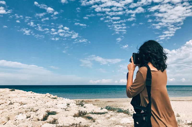 Rear view of woman photographing sea against sky