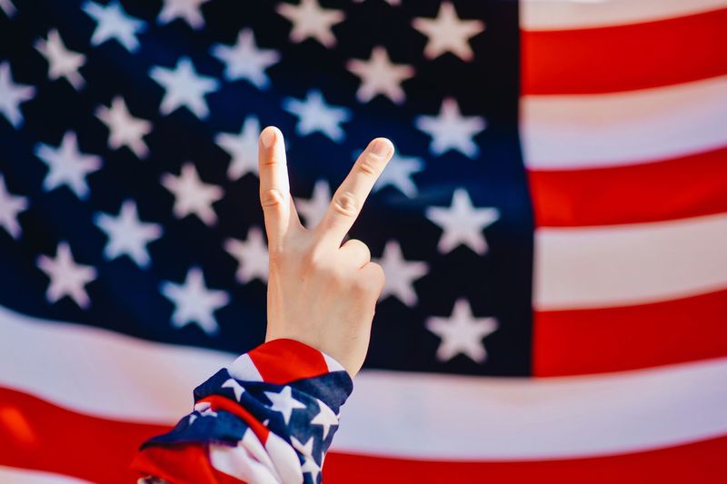 Cropped image of hand showing peace sign against american flag