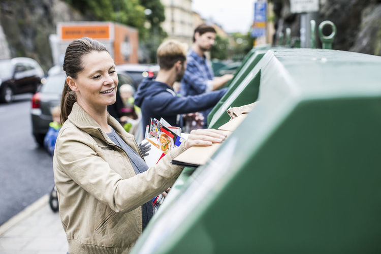 Woman and friends putting recyclable materials into recycling bins