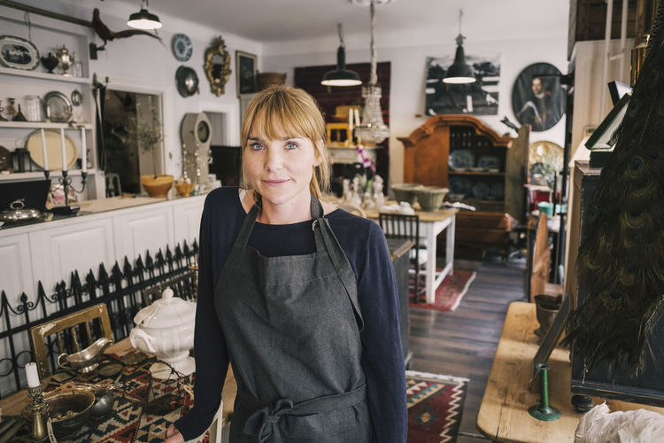 Portrait of confident owner standing by table in antique store