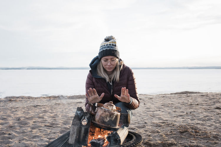 Woman warming her hands on a camp fire waiting for water to boil