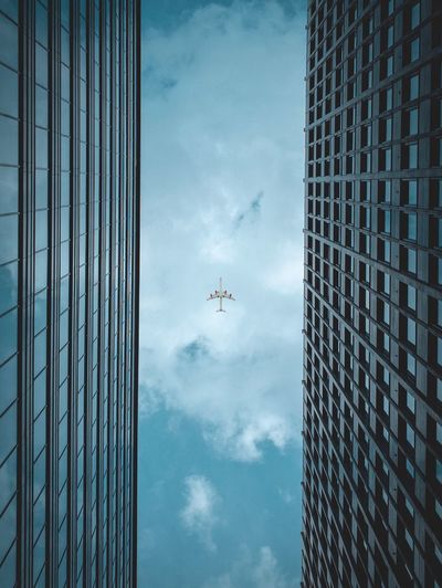 Low angle view of airplane flying over modern building against cloudy sky