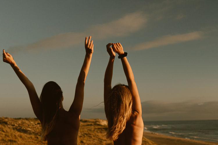 Women with arms raised standing on beach against sky