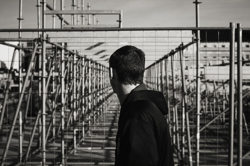 Rear view of man standing by railing against sky