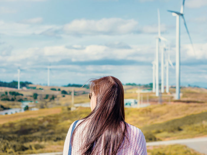 Rear view of woman standing against windmills on landscape
