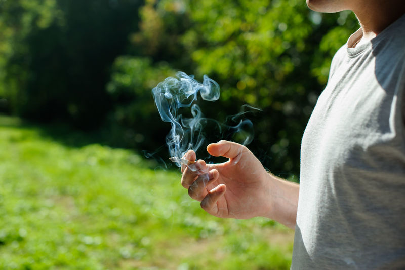Midsection of woman holding burning cigarette against trees